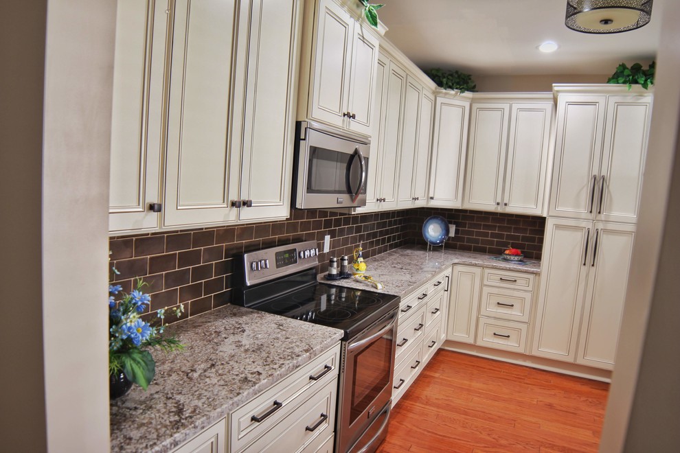 Kitchen - mid-sized u-shaped medium tone wood floor and brown floor kitchen idea in Charleston with an undermount sink, raised-panel cabinets, beige cabinets, granite countertops, brown backsplash, ceramic backsplash, stainless steel appliances and beige countertops