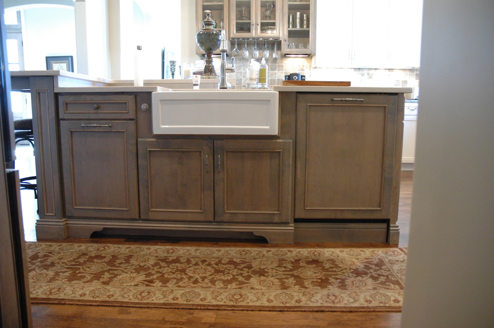 Large transitional u-shaped medium tone wood floor kitchen pantry photo with a farmhouse sink, flat-panel cabinets, white cabinets, granite countertops, brown backsplash, stone tile backsplash, paneled appliances and an island