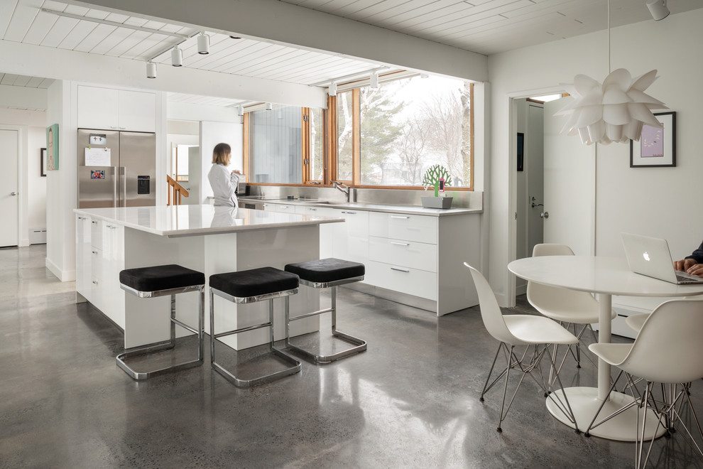 Photo of a midcentury eat-in kitchen in Portland Maine with a single-bowl sink, flat-panel cabinets, white cabinets, window splashback, stainless steel appliances, concrete floors, with island and grey floor.