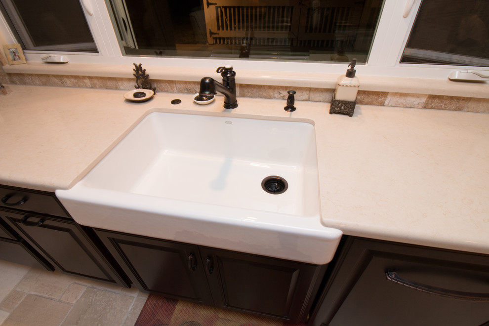 Photo of a large transitional galley open plan kitchen in Other with a farmhouse sink, raised-panel cabinets, dark wood cabinets, quartz benchtops, beige splashback, stone tile splashback, stainless steel appliances, travertine floors and with island.