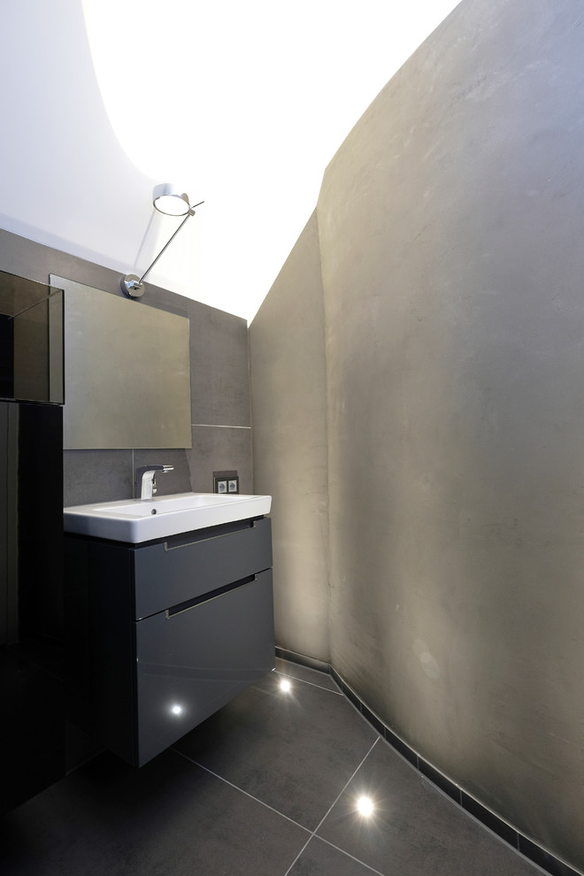 Small contemporary 3/4 bathroom in Dortmund with flat-panel cabinets, gray tile, grey floor, black cabinets, a curbless shower, a two-piece toilet, grey walls, an undermount sink, a sliding shower screen and black benchtops.