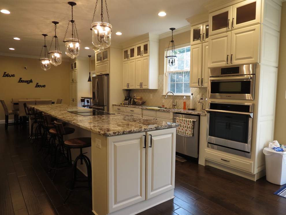 Kitchen - large transitional galley dark wood floor and brown floor kitchen idea with a double-bowl sink, raised-panel cabinets, white cabinets, granite countertops, white backsplash, porcelain backsplash, stainless steel appliances and an island