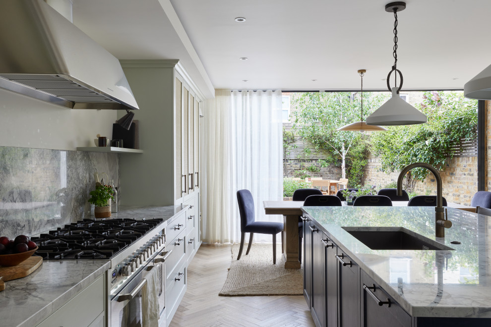 This is an example of a mid-sized transitional galley eat-in kitchen in London with shaker cabinets, green cabinets, granite benchtops, granite splashback, stainless steel appliances, light hardwood floors, with island and grey benchtop.