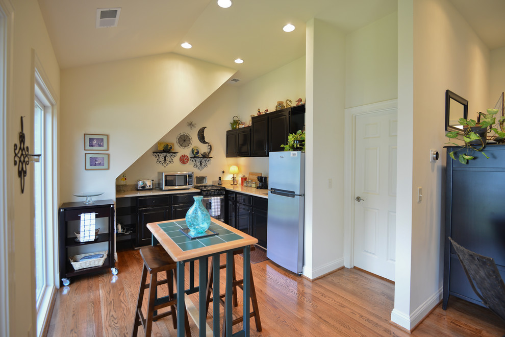 Example of a small l-shaped medium tone wood floor open concept kitchen design in DC Metro with an undermount sink, raised-panel cabinets, black cabinets, quartz countertops and stainless steel appliances