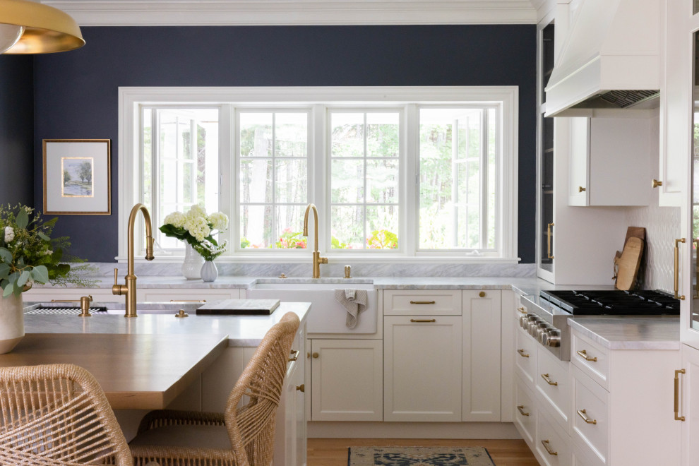 Design ideas for a mid-sized traditional l-shaped eat-in kitchen in Portland Maine with a farmhouse sink, flat-panel cabinets, white cabinets, marble benchtops, white splashback, ceramic splashback, stainless steel appliances, light hardwood floors, with island and blue benchtop.