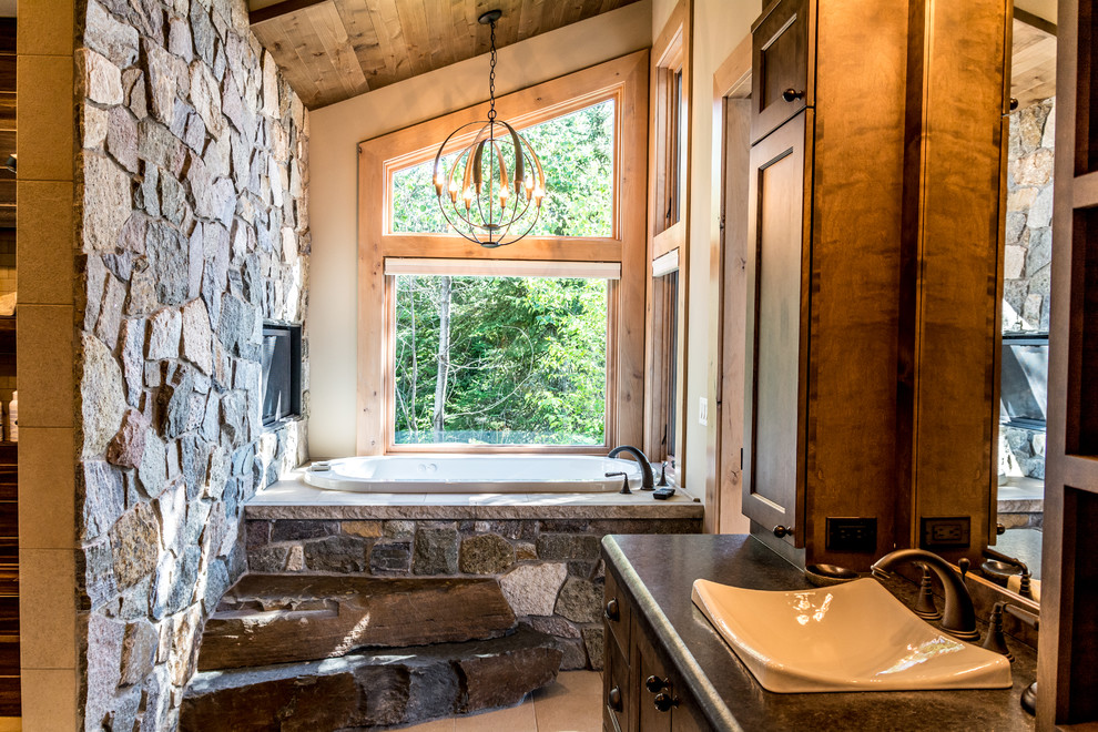Photo of a country bathroom in Other with recessed-panel cabinets, dark wood cabinets, a drop-in tub, gray tile, white walls, a drop-in sink, beige floor and grey benchtops.