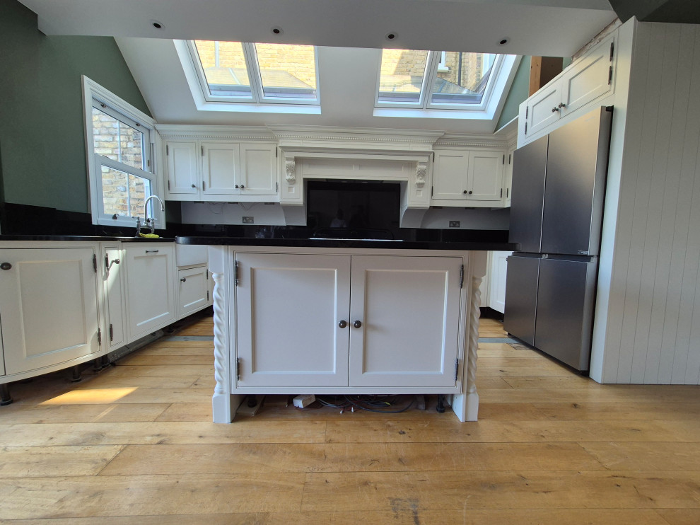 Large traditional l-shaped open plan kitchen in London with shaker cabinets, beige cabinets, granite worktops, green splashback, stainless steel appliances, dark hardwood flooring, an island, brown floors, black worktops and a vaulted ceiling.