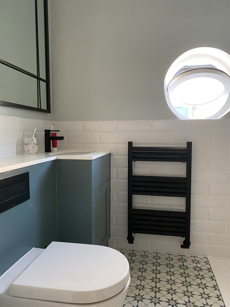 This is an example of a mid-sized contemporary kids bathroom in London with shaker cabinets, blue cabinets, a drop-in tub, a shower/bathtub combo, a wall-mount toilet, white tile, green walls, ceramic floors, quartzite benchtops, an open shower, white benchtops, a single vanity and a built-in vanity.