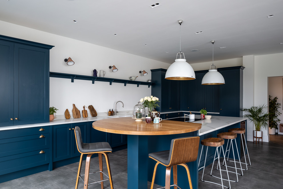 Inspiration for a transitional separate kitchen in Hertfordshire with an undermount sink, shaker cabinets, blue cabinets, concrete floors, with island, grey floor and white benchtop.