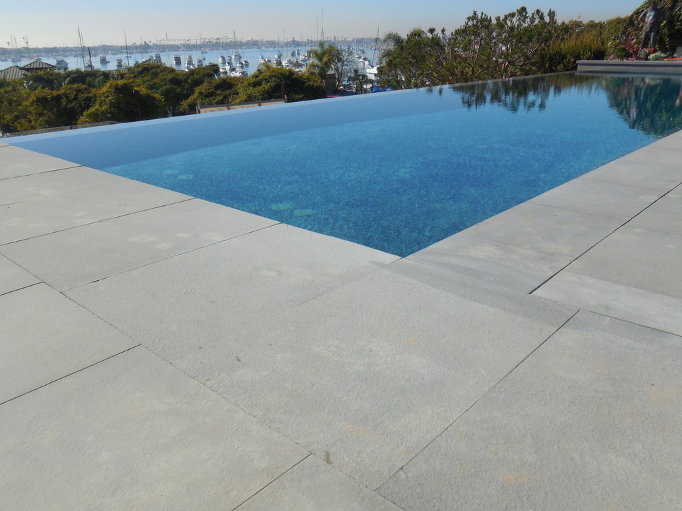 Design ideas for a large contemporary backyard custom-shaped infinity pool in Orange County with natural stone pavers.