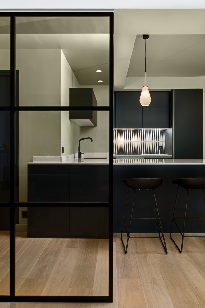 Small contemporary u-shaped eat-in kitchen in Paris with an integrated sink, flat-panel cabinets, black cabinets, quartzite benchtops, white splashback, cement tile splashback, panelled appliances and a peninsula.