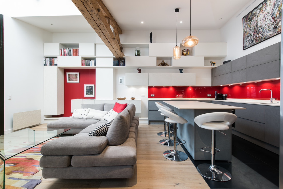 Photo of a contemporary l-shaped open plan kitchen in Paris with an undermount sink, flat-panel cabinets, grey cabinets, red splashback, glass sheet splashback, with island, black floor and white benchtop.