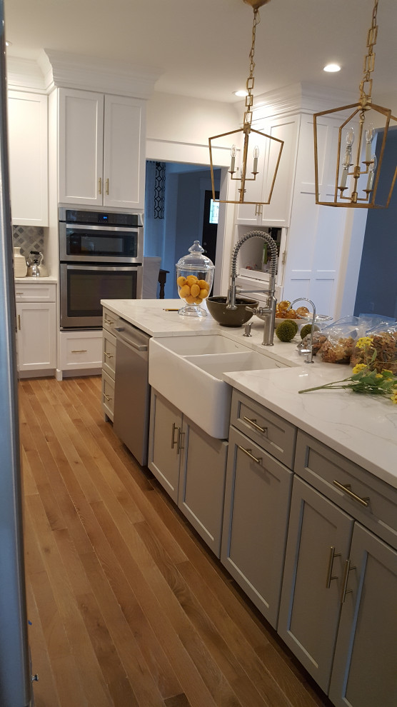 Example of a large transitional u-shaped light wood floor and brown floor eat-in kitchen design in DC Metro with a farmhouse sink, recessed-panel cabinets, white cabinets, quartzite countertops, gray backsplash, marble backsplash, stainless steel appliances, an island and white countertops