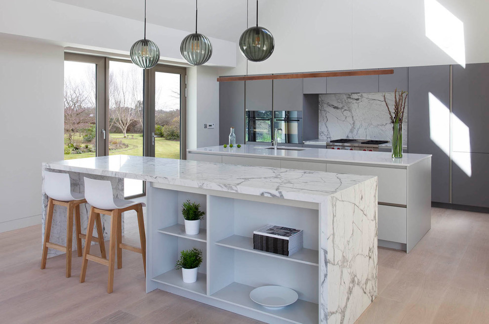 This is an example of a large contemporary single-wall open plan kitchen in Other with an integrated sink, flat-panel cabinets, green cabinets, marble benchtops, grey splashback, marble splashback, black appliances, light hardwood floors, multiple islands and brown floor.