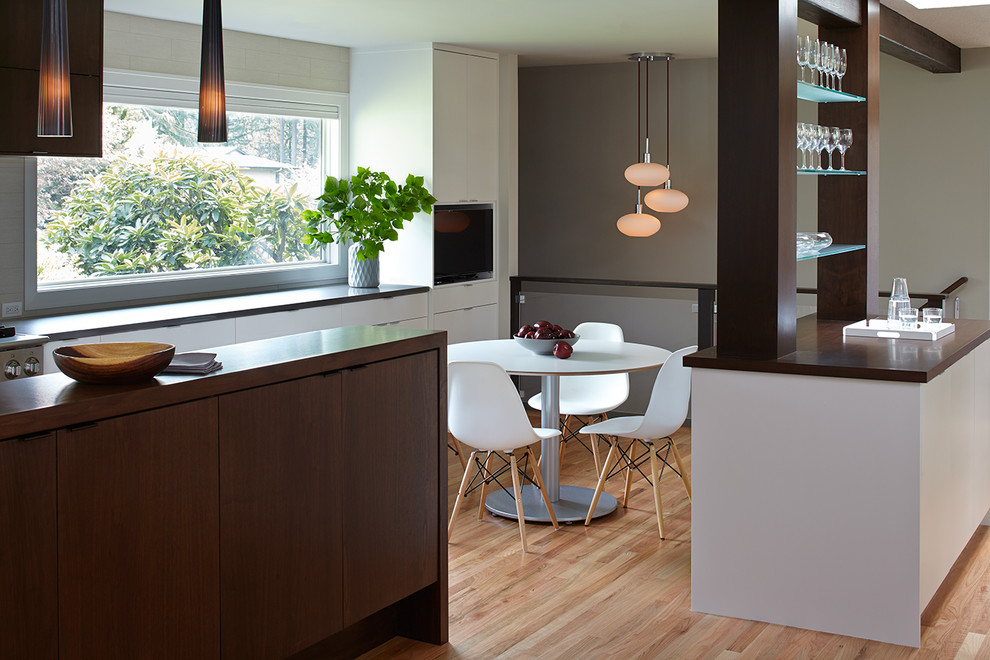 Design ideas for a large midcentury l-shaped eat-in kitchen in Portland with an undermount sink, flat-panel cabinets, dark wood cabinets, quartzite benchtops, white splashback, porcelain splashback, stainless steel appliances, light hardwood floors and with island.