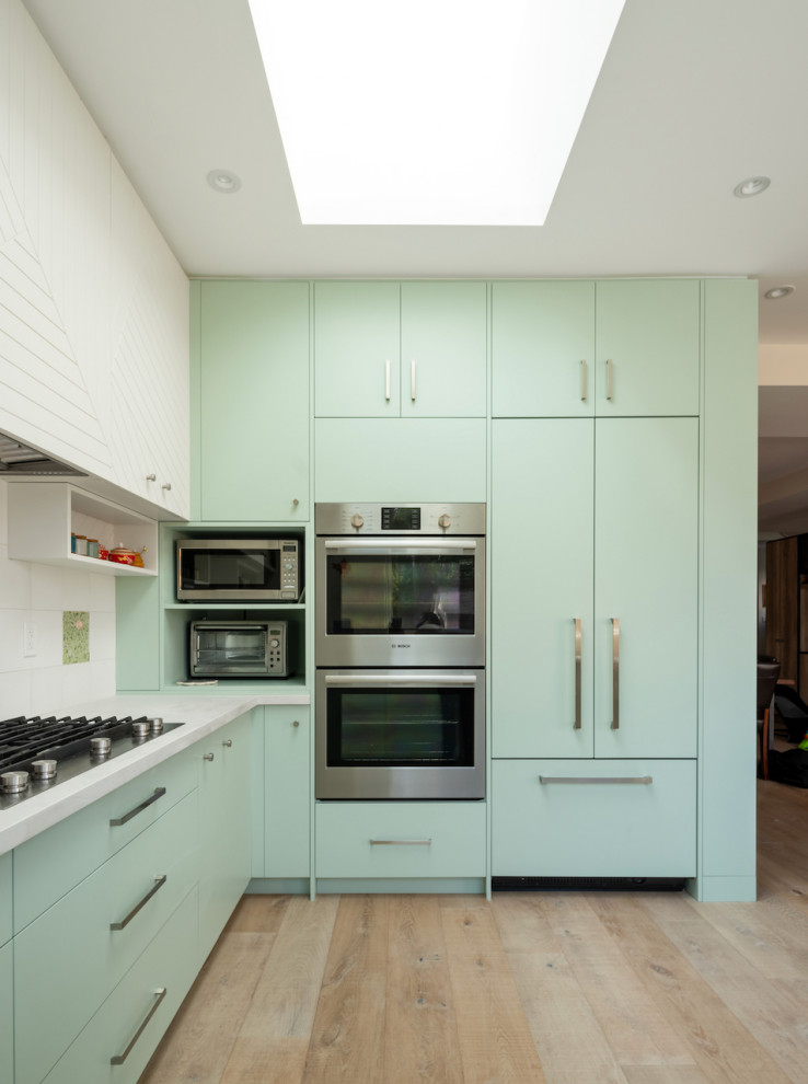 Inspiration for a large contemporary u-shaped kitchen pantry in Toronto with flat-panel cabinets, green cabinets, limestone benchtops, white splashback, ceramic splashback, stainless steel appliances, medium hardwood floors, with island, brown floor and white benchtop.