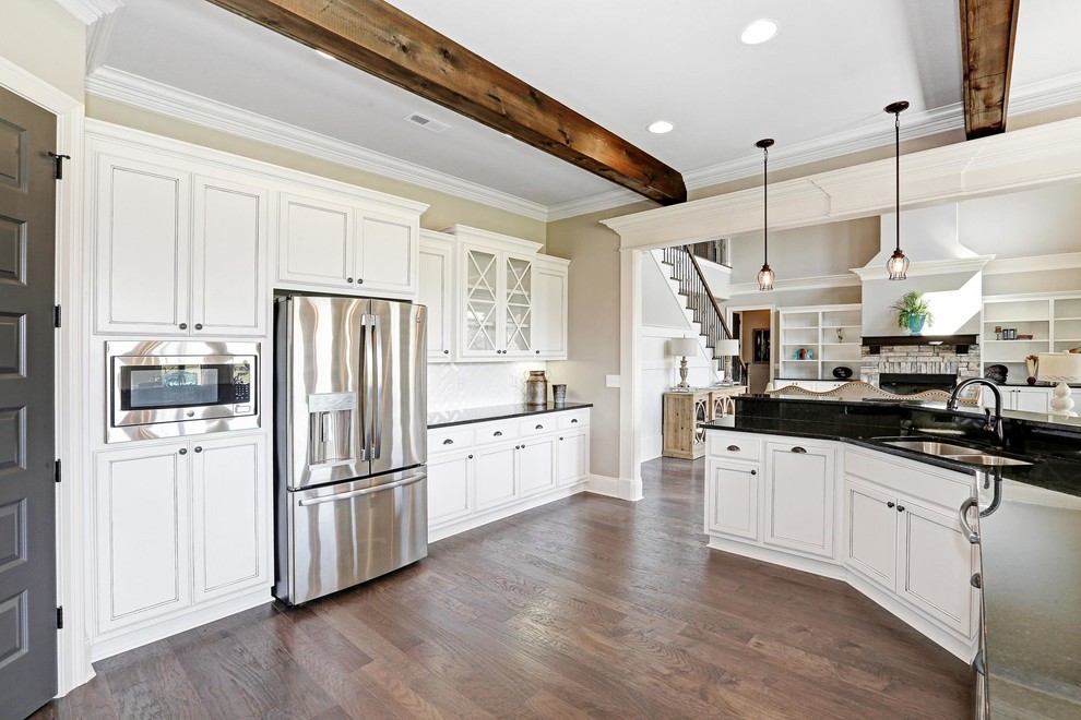 Open concept kitchen - large transitional l-shaped medium tone wood floor and brown floor open concept kitchen idea with a double-bowl sink, recessed-panel cabinets, white cabinets, quartz countertops, white backsplash, subway tile backsplash, stainless steel appliances, an island and black countertops