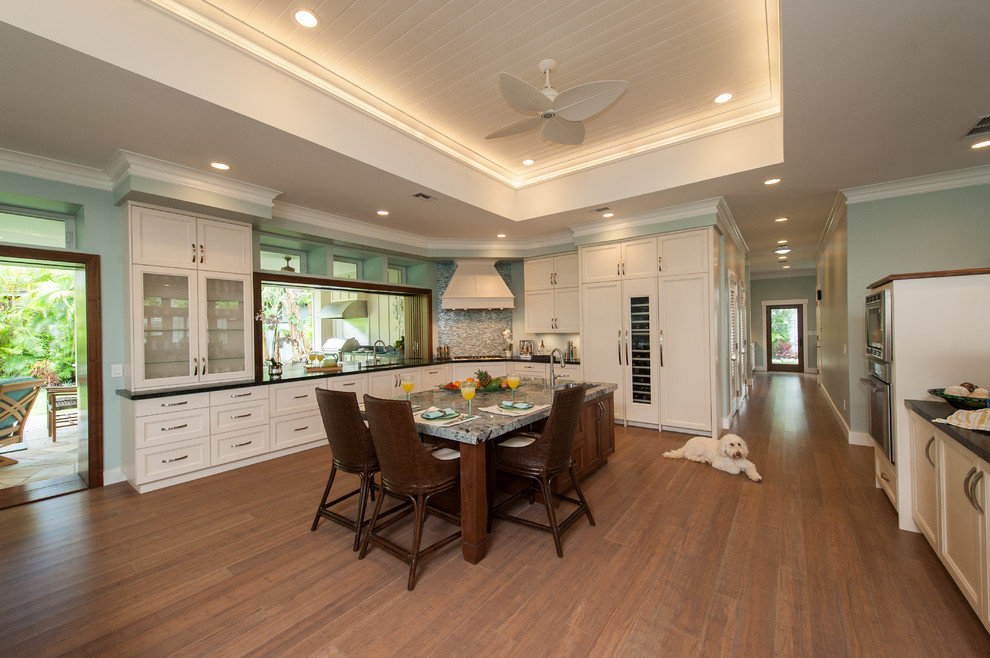 Photo of a large transitional l-shaped open plan kitchen in Hawaii with an undermount sink, shaker cabinets, white cabinets, soapstone benchtops, blue splashback, glass sheet splashback, panelled appliances, bamboo floors and with island.