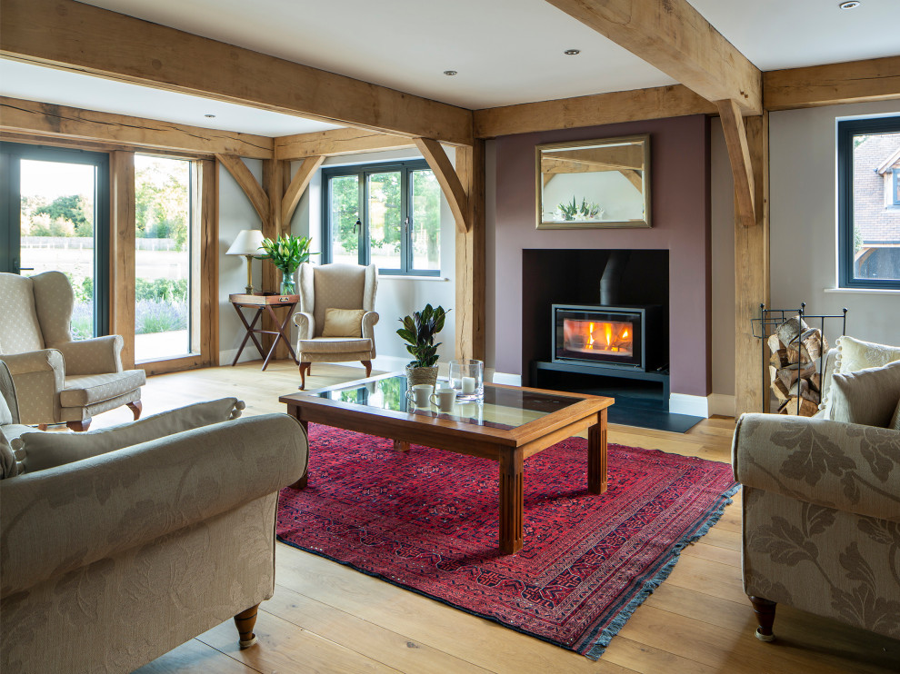 Inspiration for a small farmhouse formal and grey and purple open plan living room in Surrey with multi-coloured walls, light hardwood flooring, a wood burning stove, a plastered fireplace surround, no tv, brown floors, exposed beams and a chimney breast.