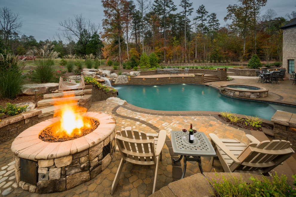 Photo of a large transitional backyard custom-shaped natural pool in Charlotte with a hot tub and brick pavers.