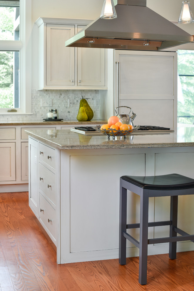Large traditional l-shaped open plan kitchen in Portland Maine with an undermount sink, recessed-panel cabinets, white cabinets, granite benchtops, beige splashback, stainless steel appliances, medium hardwood floors and with island.