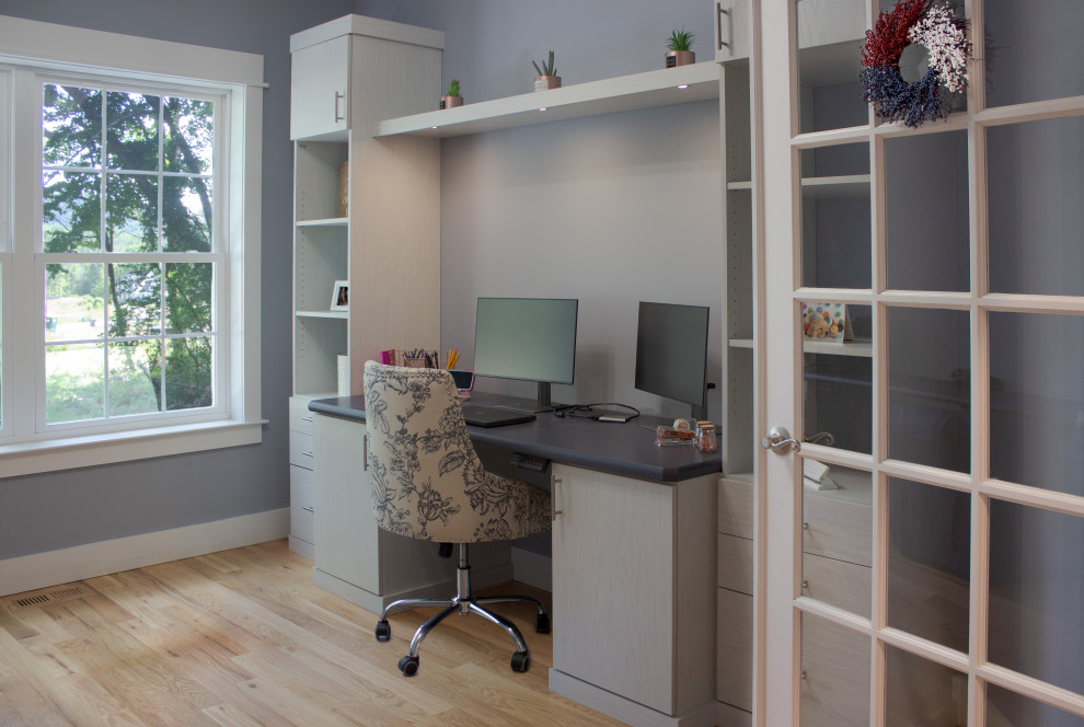 Design ideas for a mid-sized transitional home office in New York with blue walls, light hardwood floors and a built-in desk.