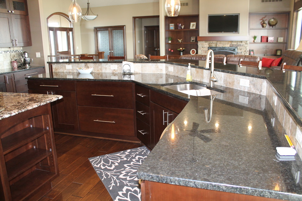 Open concept kitchen - large single-wall dark wood floor open concept kitchen idea with an undermount sink, flat-panel cabinets, dark wood cabinets, granite countertops, beige backsplash, stainless steel appliances, beige walls and two islands
