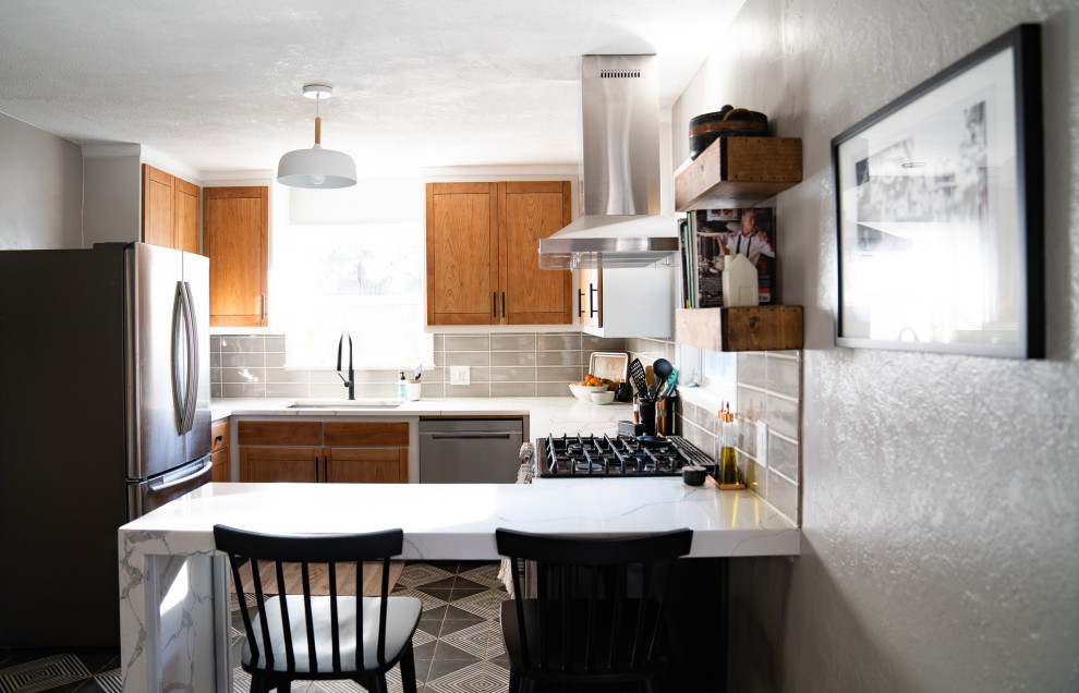 Small transitional u-shaped ceramic tile and black floor eat-in kitchen photo with an undermount sink, flat-panel cabinets, light wood cabinets, quartz countertops, gray backsplash, porcelain backsplash, stainless steel appliances and white countertops