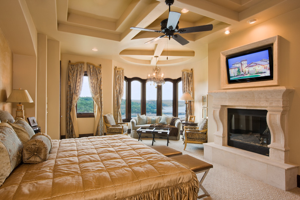 This is an example of a large mediterranean master bedroom in Austin with beige walls, carpet, a standard fireplace, a stone fireplace surround and beige floor.