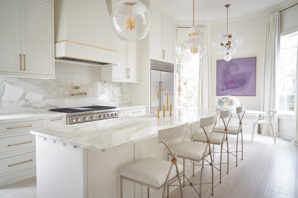 This is an example of a large transitional l-shaped eat-in kitchen in New Orleans with a farmhouse sink, shaker cabinets, white cabinets, marble benchtops, white splashback, marble splashback, stainless steel appliances, light hardwood floors, with island, white floor and white benchtop.