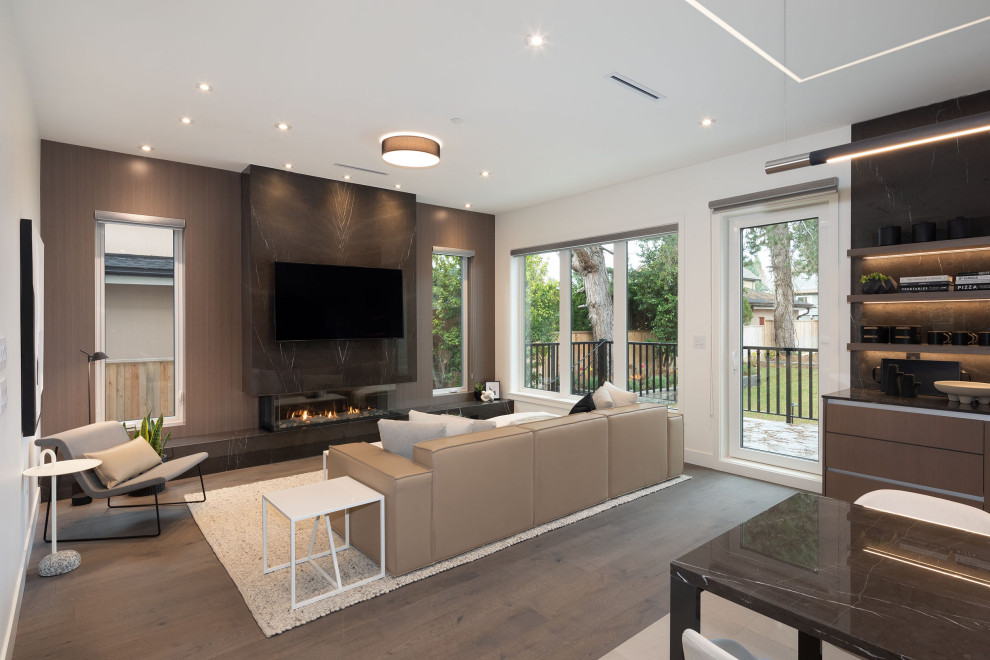 Inspiration for a medium sized modern open plan games room in Vancouver with black walls, medium hardwood flooring, a standard fireplace, a tiled fireplace surround, a wall mounted tv and brown floors.