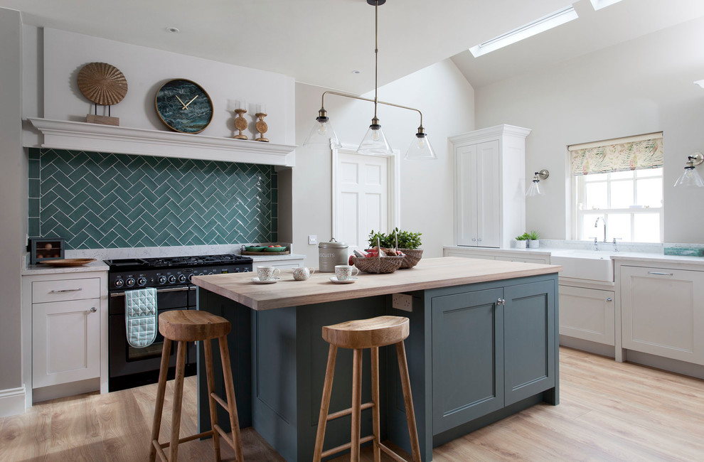 This is an example of a country l-shaped kitchen in Other with a farmhouse sink, recessed-panel cabinets, green cabinets, wood benchtops, green splashback, black appliances, medium hardwood floors, with island, beige floor and beige benchtop.