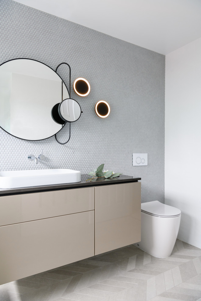 This is an example of a contemporary 3/4 bathroom in Hobart with flat-panel cabinets, beige cabinets, a one-piece toilet, gray tile, mosaic tile, white walls, a vessel sink, engineered quartz benchtops, multi-coloured floor, black benchtops, a single vanity and a floating vanity.