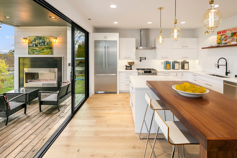 Design ideas for a contemporary eat-in kitchen in Seattle with an undermount sink, flat-panel cabinets, white cabinets, white splashback, stainless steel appliances, light hardwood floors, with island, beige floor and white benchtop.
