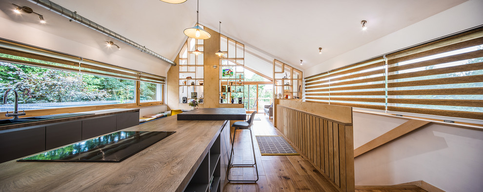 Photo of a mid-sized contemporary galley open plan kitchen in Other with a double-bowl sink, grey cabinets, wood benchtops, window splashback, medium hardwood floors, with island, brown floor, brown benchtop, flat-panel cabinets and vaulted.