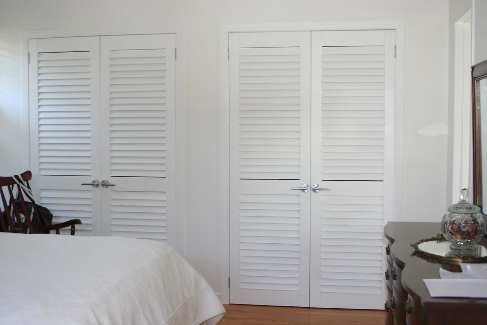 Inspiration for a mid-sized traditional gender-neutral built-in wardrobe in Toronto with louvered cabinets, white cabinets, medium hardwood floors and brown floor.