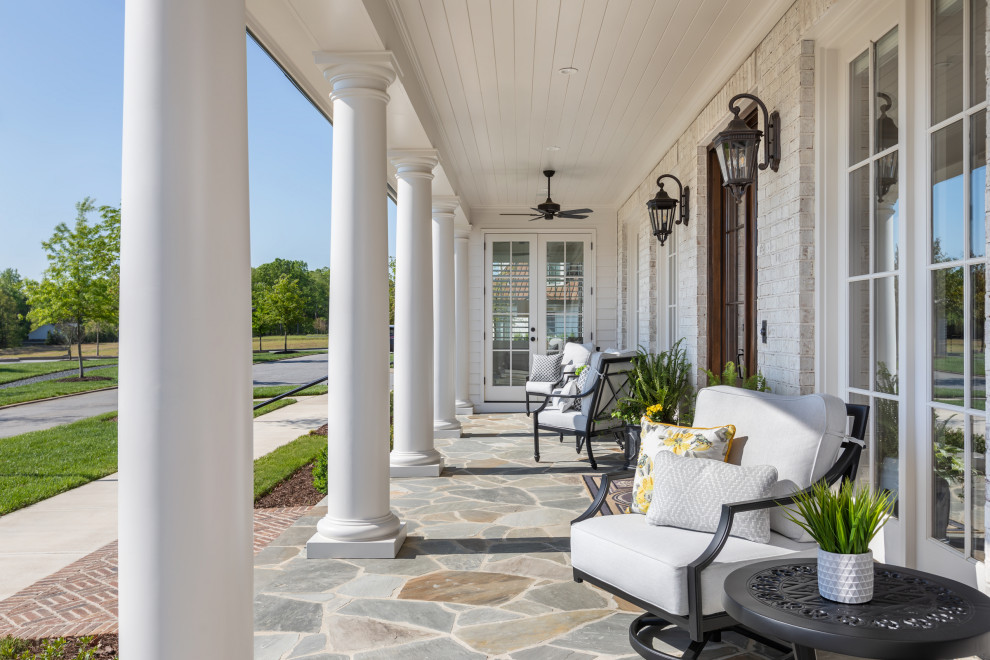 This is an example of a large traditional front veranda in Atlanta with with columns, natural stone paving and a roof extension.