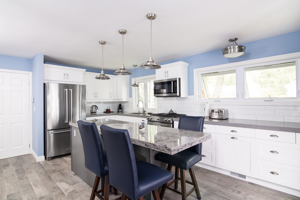 Example of a mid-sized transitional l-shaped light wood floor enclosed kitchen design with an undermount sink, beaded inset cabinets, white cabinets, granite countertops, white backsplash, ceramic backsplash, stainless steel appliances and an island