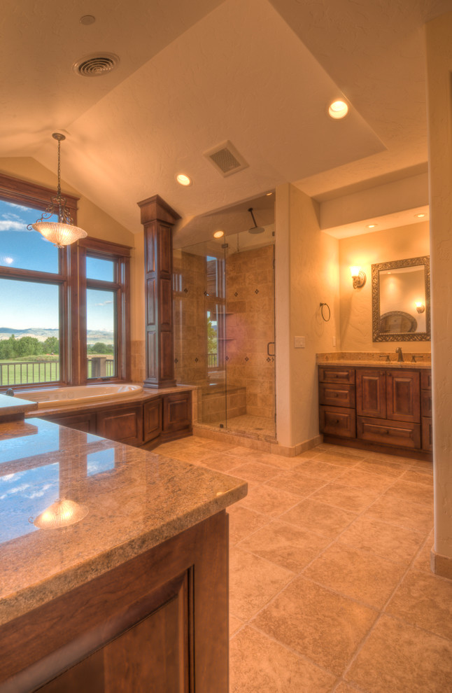 Photo of a large country master bathroom in Denver with an undermount sink, raised-panel cabinets, medium wood cabinets, granite benchtops, a drop-in tub, an alcove shower, a two-piece toilet, beige tile, stone tile, beige walls and travertine floors.