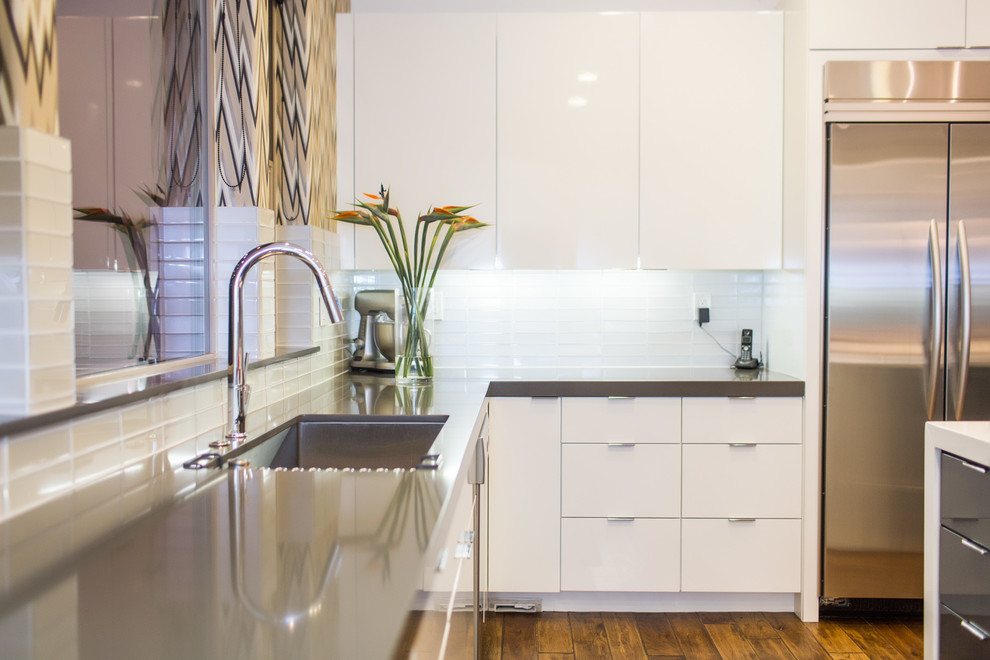 This is an example of a modern kitchen in Sacramento with an undermount sink, flat-panel cabinets, white cabinets, solid surface benchtops, metallic splashback, glass tile splashback, stainless steel appliances and medium hardwood floors.