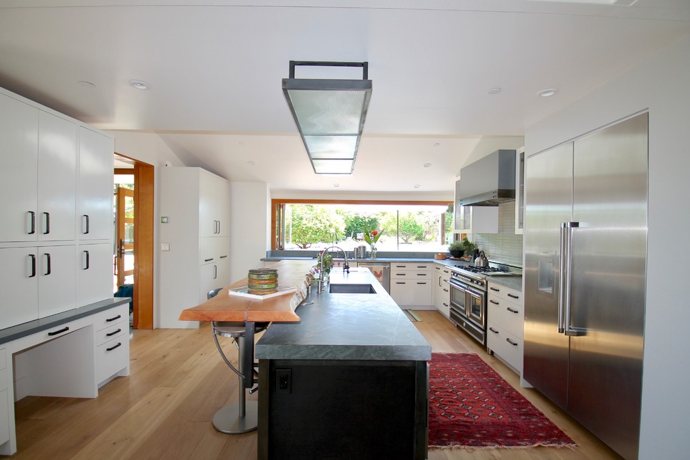 This is an example of a transitional l-shaped separate kitchen in San Francisco with a single-bowl sink, flat-panel cabinets, white cabinets, window splashback, stainless steel appliances, light hardwood floors, with island and beige floor.