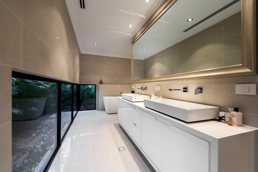 Inspiration for a large contemporary master bathroom in Perth with white cabinets, a freestanding tub, porcelain tile, porcelain floors, a vessel sink, engineered quartz benchtops, beige floor, beige benchtops, flat-panel cabinets and gray tile.