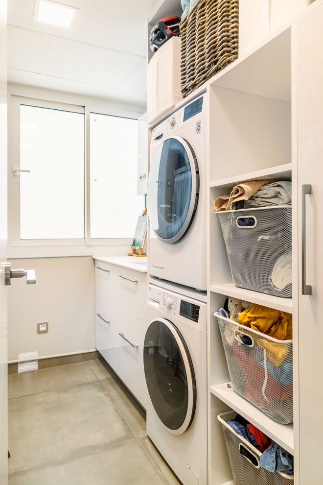This is an example of a contemporary single-wall laundry room in Other with flat-panel cabinets, white cabinets, white walls, a stacked washer and dryer, grey floor and white benchtop.