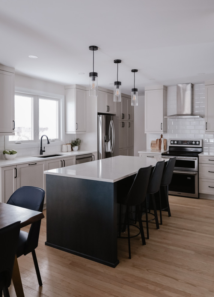 Inspiration for a mid-sized transitional l-shaped light wood floor and brown floor eat-in kitchen remodel with an undermount sink, shaker cabinets, beige cabinets, quartz countertops, white backsplash, subway tile backsplash, stainless steel appliances, an island and white countertops