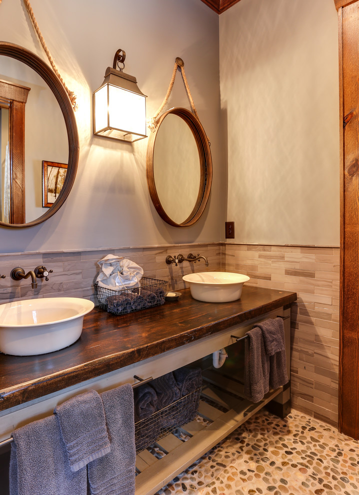 Design ideas for a mid-sized country bathroom in Raleigh with furniture-like cabinets, distressed cabinets, a two-piece toilet, gray tile, subway tile, grey walls, pebble tile floors, a vessel sink, wood benchtops and multi-coloured floor.