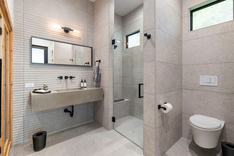 Mid-sized modern master bathroom in Houston with an alcove shower, a wall-mount toilet, gray tile, grey walls, a wall-mount sink, concrete benchtops, beige floor, a hinged shower door, grey benchtops, a shower seat, a single vanity and a floating vanity.