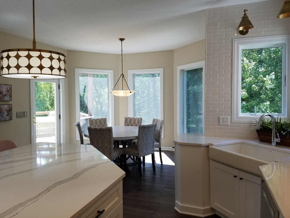 Example of a large transitional u-shaped medium tone wood floor and gray floor eat-in kitchen design with a farmhouse sink, shaker cabinets, white cabinets, quartz countertops, white backsplash, subway tile backsplash, stainless steel appliances, an island and white countertops