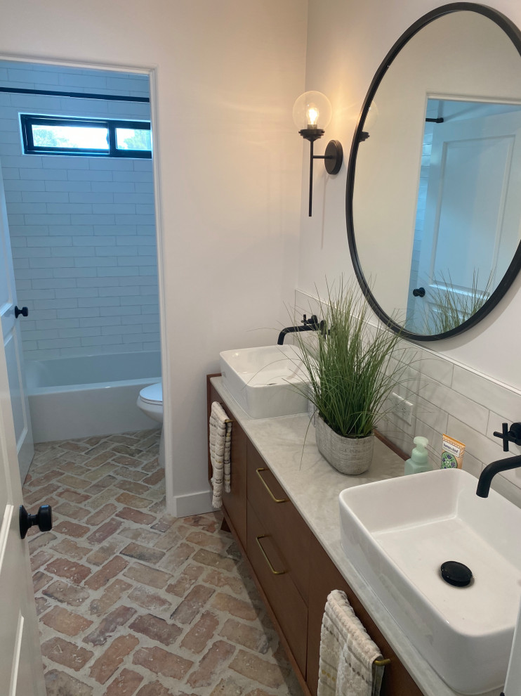 Medium sized traditional family bathroom in Los Angeles with flat-panel cabinets, medium wood cabinets, an alcove bath, a shower/bath combination, a one-piece toilet, white tiles, ceramic tiles, white walls, brick flooring, a vessel sink, granite worktops, red floors, a shower curtain, white worktops, double sinks and a freestanding vanity unit.