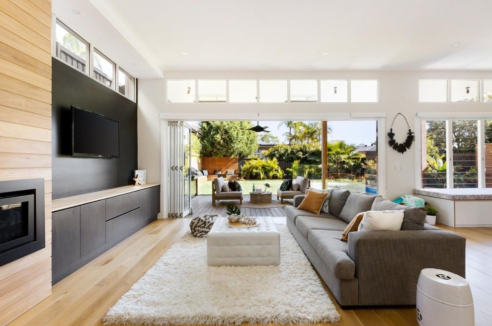 This is an example of a contemporary open concept living room in Sydney with black walls, light hardwood floors, a wall-mounted tv and beige floor.