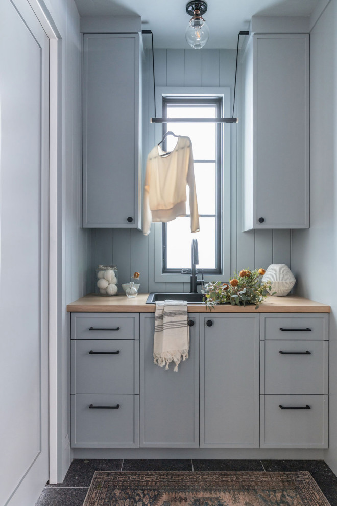 Design ideas for a mid-sized beach style galley utility room in Portland with a drop-in sink, recessed-panel cabinets, blue cabinets, wood benchtops, blue splashback, timber splashback, blue walls, limestone floors, black floor and panelled walls.